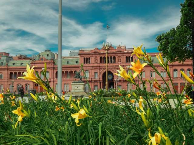 Foto da casa rosada em Buenos Aires. Flores amarelas na frente do edifício rosa.