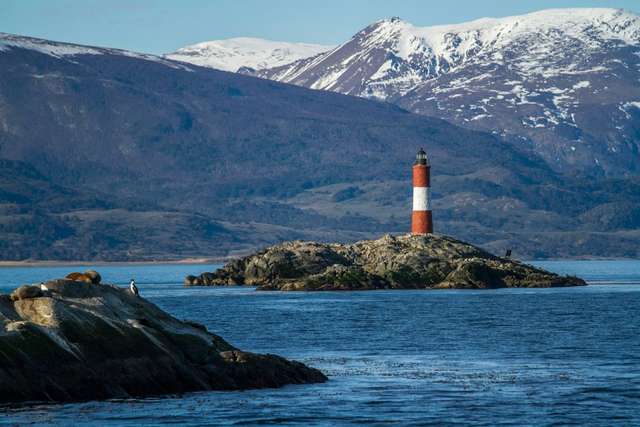 Ushuaia. Farol vermelho e branco em uma ilha e montanhas ao fundo