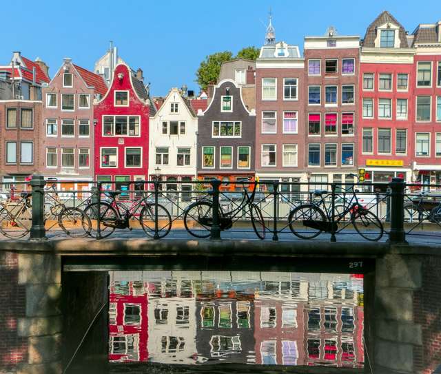 Bicicletas apoiadas em uma cerca com edifícios coloridos no fundo.