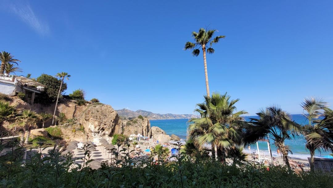 Foto Nerja. Paisagem de dia com vegetação verde, praia e mar azul.