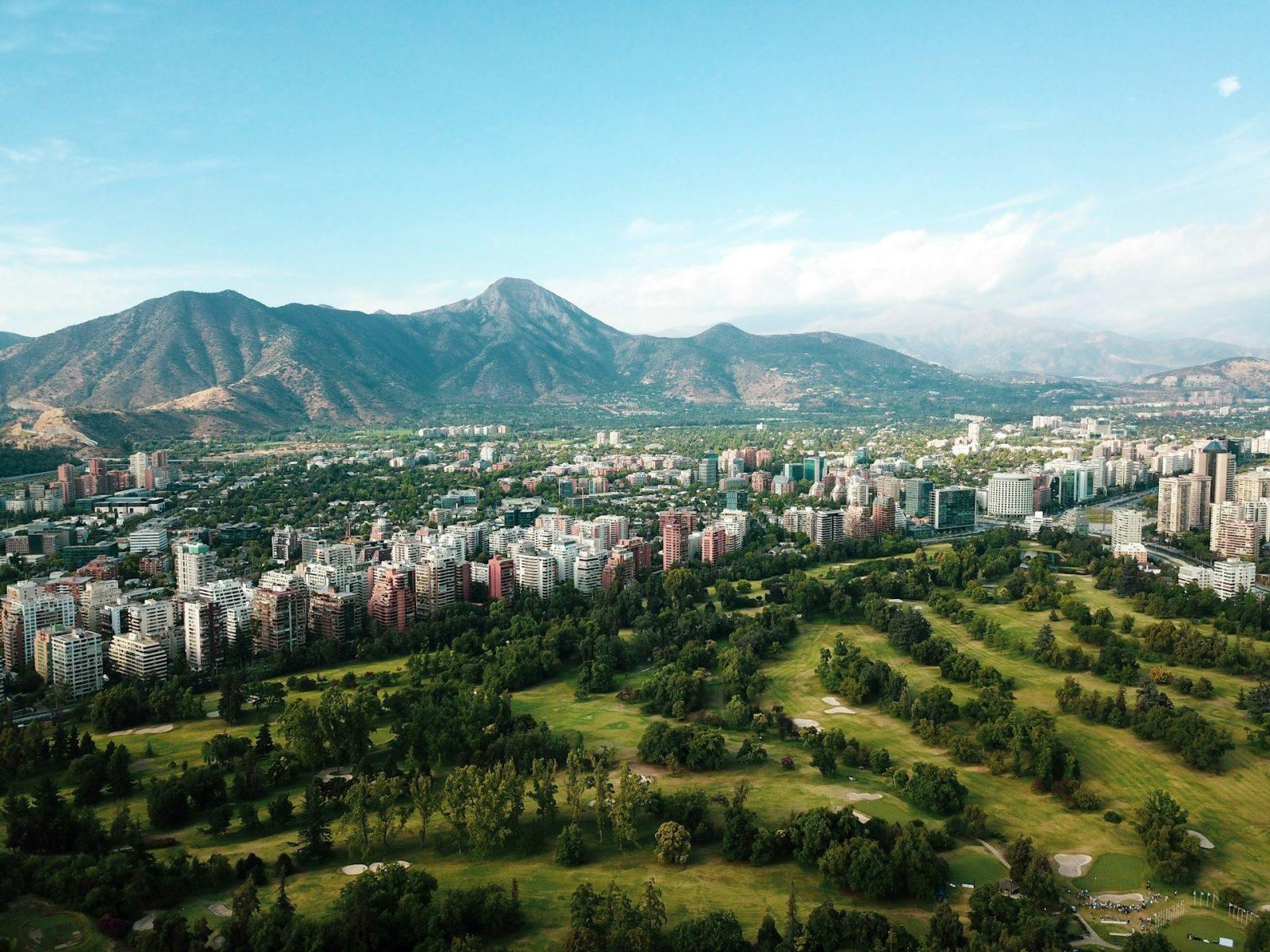 Foto de Santiago do Chile. Paisagem com gramado, edifícios ao redor e montanhas ao fundo.