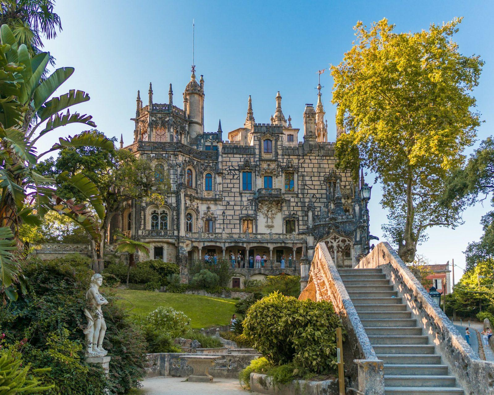 Foto palácio em Sintra. edifício de concreto, uma escadaria e arvores verdes.